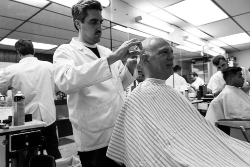 A barber at Andre's gives a customer a haircut, with mirrors reflecting the length of the shop.