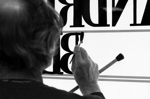 A sign painter hand-letters the storefront window.